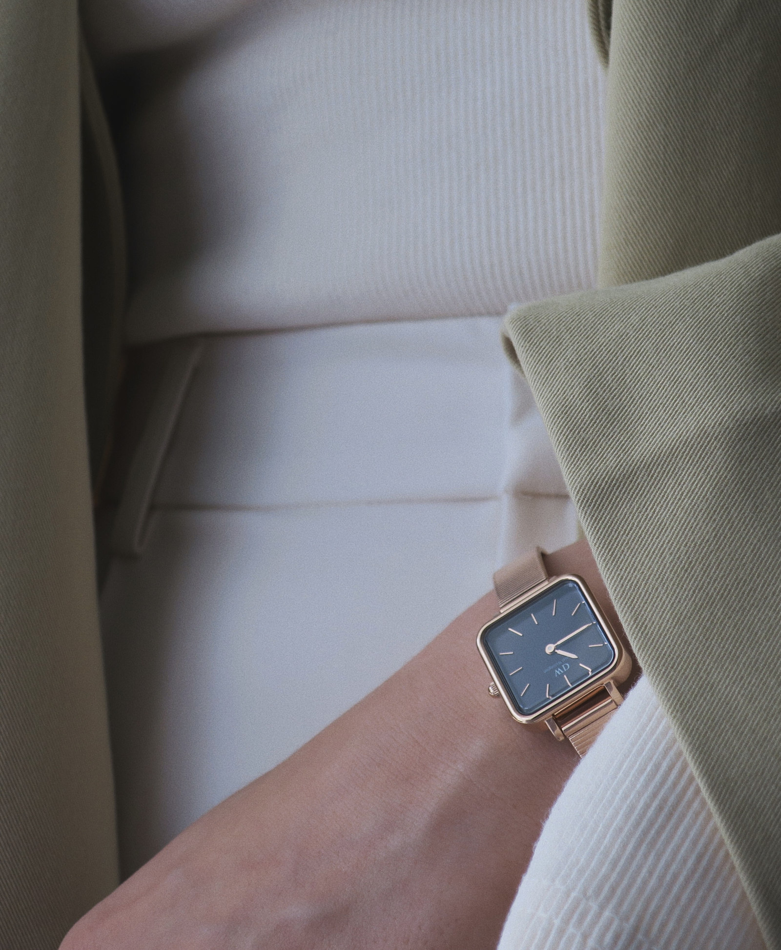 Złoty zegarek Daniel Wellington z ciemną tarczą przy zielonej marynarce